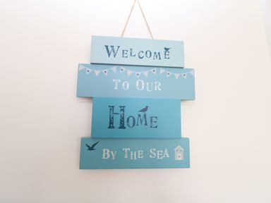 A wall hanging sign with the text welcome to our home by the sea with bird and house illustrations at 14 Siesta Mar in Mundesley