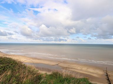 A view of a sandy beach and sea under a cloudy sky at 14 Siesta Mar in Mundesley