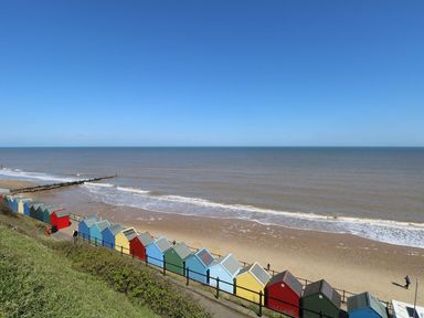 A row of colorful beach huts along a sandy shore with the sea and blue sky at 14 Siesta Mar in Mundesley