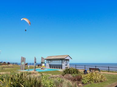 A coastal park with a shelter bench and grass near the sea with a paraglider in the sky at 14 Siesta Mar in Mundesley