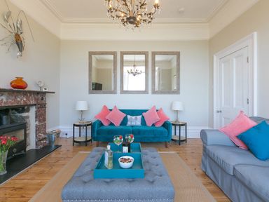 A living room with a blue sofa pink cushions gray armchair gray ottoman and a fireplace at 6 Albany Terrace in St Ives