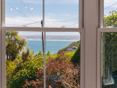 A coastal view through a window with plants and houses outside at 6 Albany Terrace in St Ives