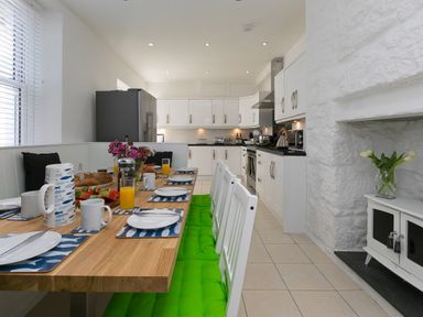 A kitchen with a wooden dining table set for breakfast and white cabinets at 6 Albany Terrace in St Ives