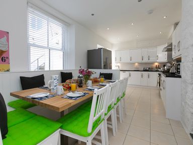 A kitchen with a wooden dining table and white chairs with green cushions at 6 Albany Terrace in St Ives
