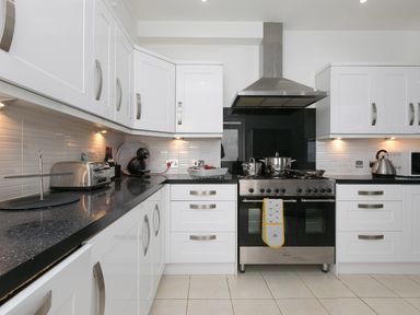 A kitchen with white cabinets black countertops a stove with pots toaster kettle and coffee machine at 6 Albany Terrace in St Ives