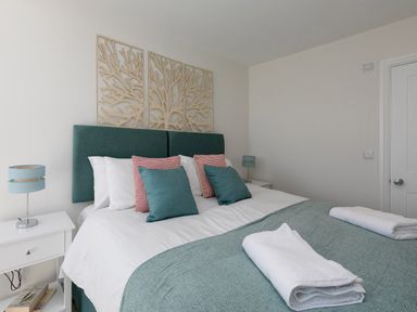 A bedroom with teal headboard two bedside tables and a bed with pillows and folded towels at 6 Albany Terrace in St Ives