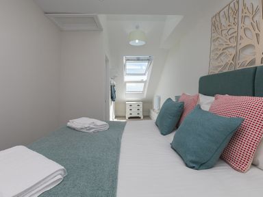 A bedroom with a bed with teal and red pillows a small white chest of drawers under skylight windows at 6 Albany Terrace in St Ives