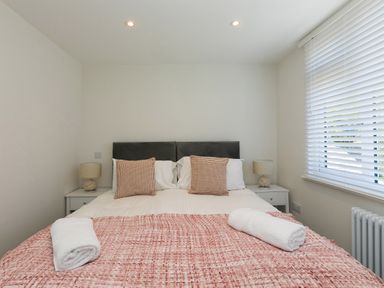 A bedroom with a bed with two pillows and two rolled towels a window with blinds two bedside tables with lamps at 6 Albany Terrace in St Ives
