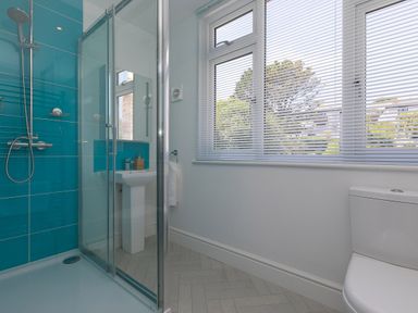 A bathroom with a glass shower enclosure blue tiled wall a pedestal sink a toilet and windows with white blinds at 6 Albany Terrace in St Ives
