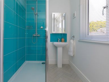 A bathroom with a walk-in shower with blue tiles a sink with a mirror above and a window with blinds at 6 Albany Terrace in St Ives