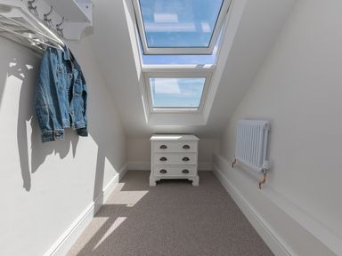 A small room with slanted ceiling windows a white chest of drawers a radiator and a blue denim jacket hanging on hooks at 6 Albany Terrace in St Ives