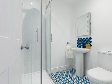 A bathroom with a glass shower enclosure a pedestal sink a mirror toilet and blue patterned floor tiles at 6 Albany Terrace in St Ives