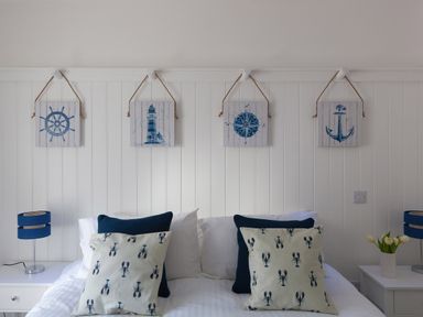 A bedroom with a white bed with cushions and nautical wall art above the headboard at 6 Albany Terrace in St Ives