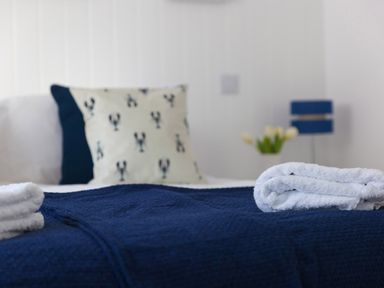 A bed with folded white towels and cushions including one with lobster designs at 6 Albany Terrace in St Ives