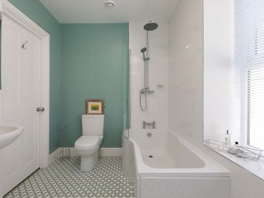A bathroom with a bathtub and shower, toilet, sink, and a window with blinds at 6 Albany Terrace in St Ives