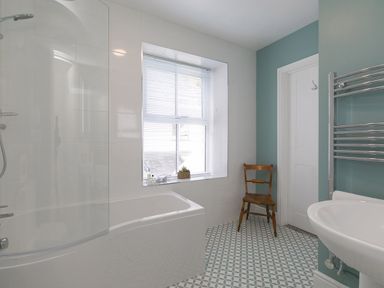 A bathroom with bathtub shower window wooden chair sink towel rack and patterned floor at 6 Albany Terrace in St Ives