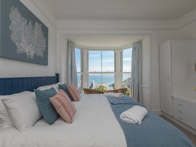 A bedroom with a bed and pillows facing a bay window with a view of the sea at 6 Albany Terrace in St Ives