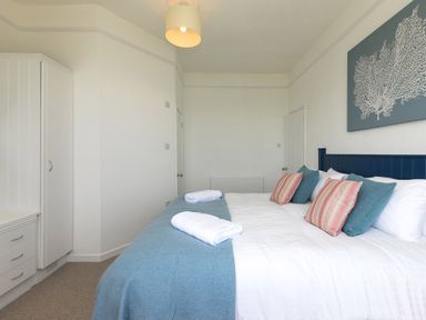 A bedroom with a bed with blue and striped pillows blue bedspread white walls and white wardrobe at 6 Albany Terrace in St Ives