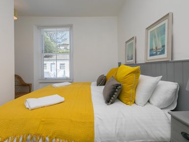 A bedroom with a bed with yellow and gray pillows and a yellow blanket by a window at 6 Albany Terrace in St Ives