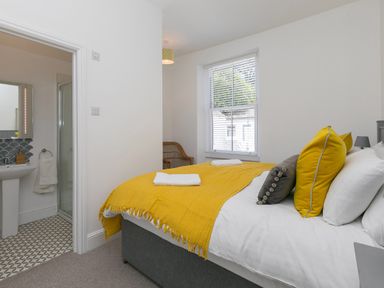 A bedroom with a bed covered in a yellow blanket and pillows and an en suite bathroom visible at 6 Albany Terrace in St Ives