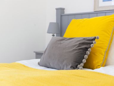 A bed with yellow and gray cushions and a yellow blanket in a bedroom at 6 Albany Terrace in St Ives