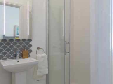 A bathroom with a pedestal sink a mirror with lights a towel ring with a white towel and a glass shower enclosure at 6 Albany Terrace in St Ives