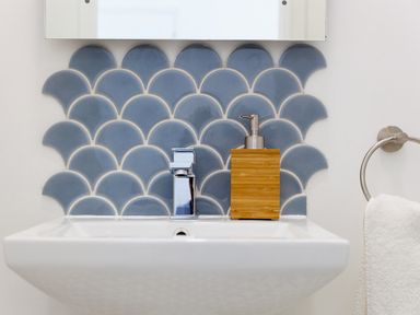 A bathroom sink with a chrome faucet wooden soap dispenser and blue fish scale tiles on the wall at 6 Albany Terrace in St Ives