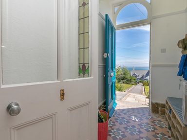 An open front door with stained glass panel and tiled floor looking out to a garden path and sea view at 6 Albany Terrace in St Ives