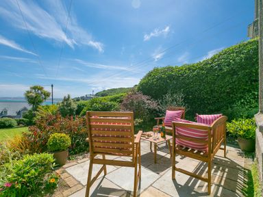 An outdoor patio with wooden chairs and a table set with drinks and snacks surrounded by plants and overlooking a garden at 6 Albany Terrace in St Ives