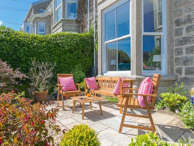 An outdoor seating area with wooden chairs and a table with cushions and plants at 6 Albany Terrace in St Ives