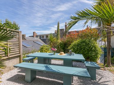 An outdoor garden area with a blue picnic table and benches surrounded by plants and buildings at 6 Albany Terrace in St Ives