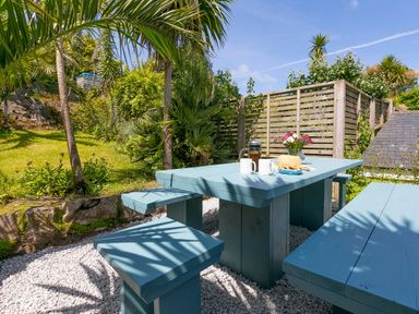 An outdoor seating area with a blue wooden picnic table and benches with coffee mugs biscuits and flowers in a garden at 6 Albany Terrace in St Ives