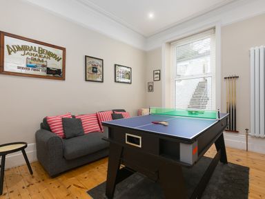 A game room with a ping pong table a gray sofa with striped cushions and framed posters on the wall at 6 Albany Terrace in St Ives