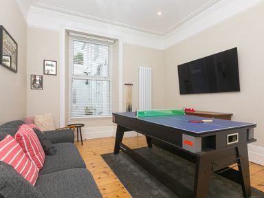 A game room with a ping pong table a sofa with striped cushions a TV mounted on the wall and windows at 6 Albany Terrace in St Ives