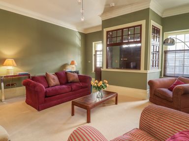 A living room with red sofas a wooden coffee table with flowers and green walls at Lion House in Moretonhampstead