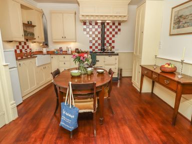 A kitchen with a wooden table set with dishes and flowers and cream cabinets with a stove and red and white tiled backsplash at Lion House in Moretonhampstead