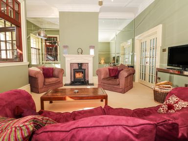 A living room with striped armchairs a red sofa a wooden coffee table and a fireplace at Lion House in Moretonhampstead