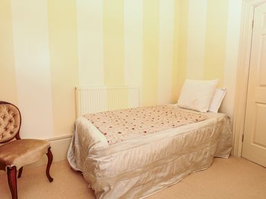 A bedroom with a striped wallpaper single bed with floral bedding and a wooden chair