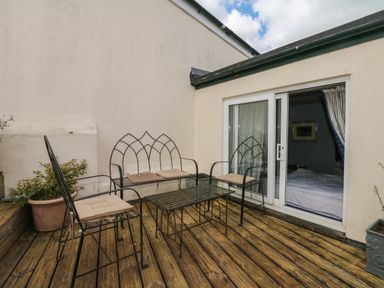 An outdoor wooden deck with black metal chairs and a table next to a sliding glass door at Lion House in Moretonhampstead