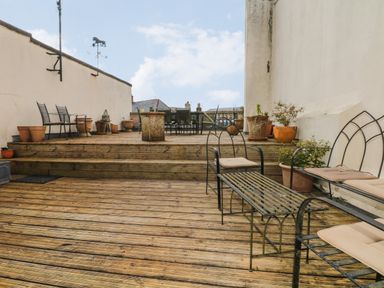 An outdoor wooden deck with metal furniture and potted plants at Lion House in Moretonhampstead