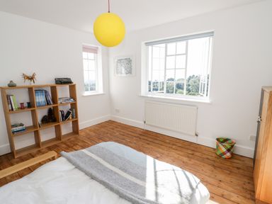 A bedroom with wooden floor a bed with a blanket a wooden shelf with books and decorative items a yellow hanging light and two windows at Tor Cottage in Colwall Herefordshire