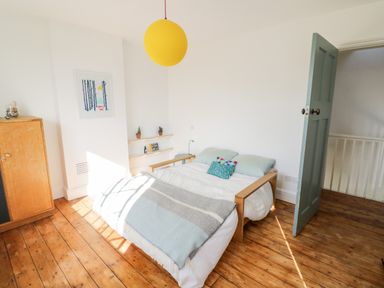 A bedroom with a double bed a wooden cabinet a yellow hanging lamp and a blue door at Tor Cottage in Colwall Herefordshire