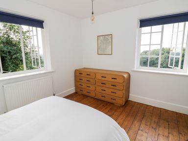A bedroom with two windows a wooden chest of drawers and a bed at Tor Cottage in Colwall Herefordshire