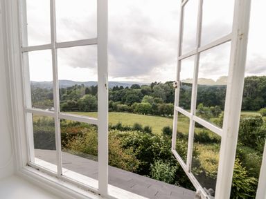 A view through white framed open windows overlooking green fields and trees at Tor Cottage in Colwall Herefordshire