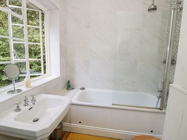 A bathroom with a sink next to a bathtub and a window showing greenery at Tor Cottage in Colwall Herefordshire