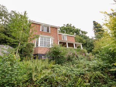 A brick house with white framed windows surrounded by green vegetation and trees at Tor Cottage in Colwall Herefordshire