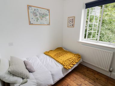 A bedroom with a single bed and yellow blanket next to a window and wooden floor at Tor Cottage in Colwall Herefordshire
