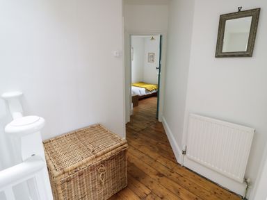 A hallway with wooden flooring a wicker basket a wall mirror and a radiator at Tor Cottage in Colwall Herefordshire
