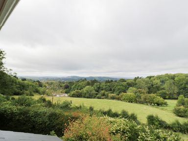 A rural landscape with green fields trees and distant hills under a cloudy sky at Tor Cottage in Colwall Herefordshire