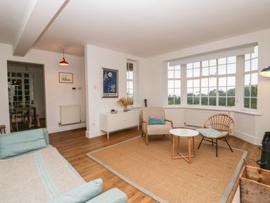 A living room with chairs and a table on a rug and large windows at Tor Cottage in Colwall Herefordshire